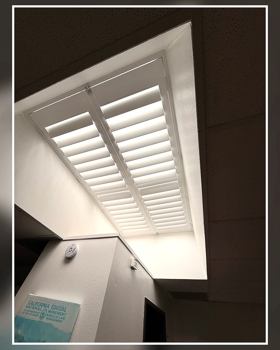 Custom white plantation shutters installed over a Ventura County skylight with the louvers open